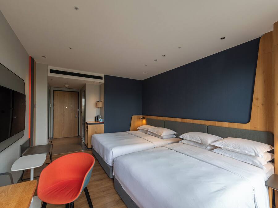 A modern hotel room with two beds, a TV, a desk, and a red chair.