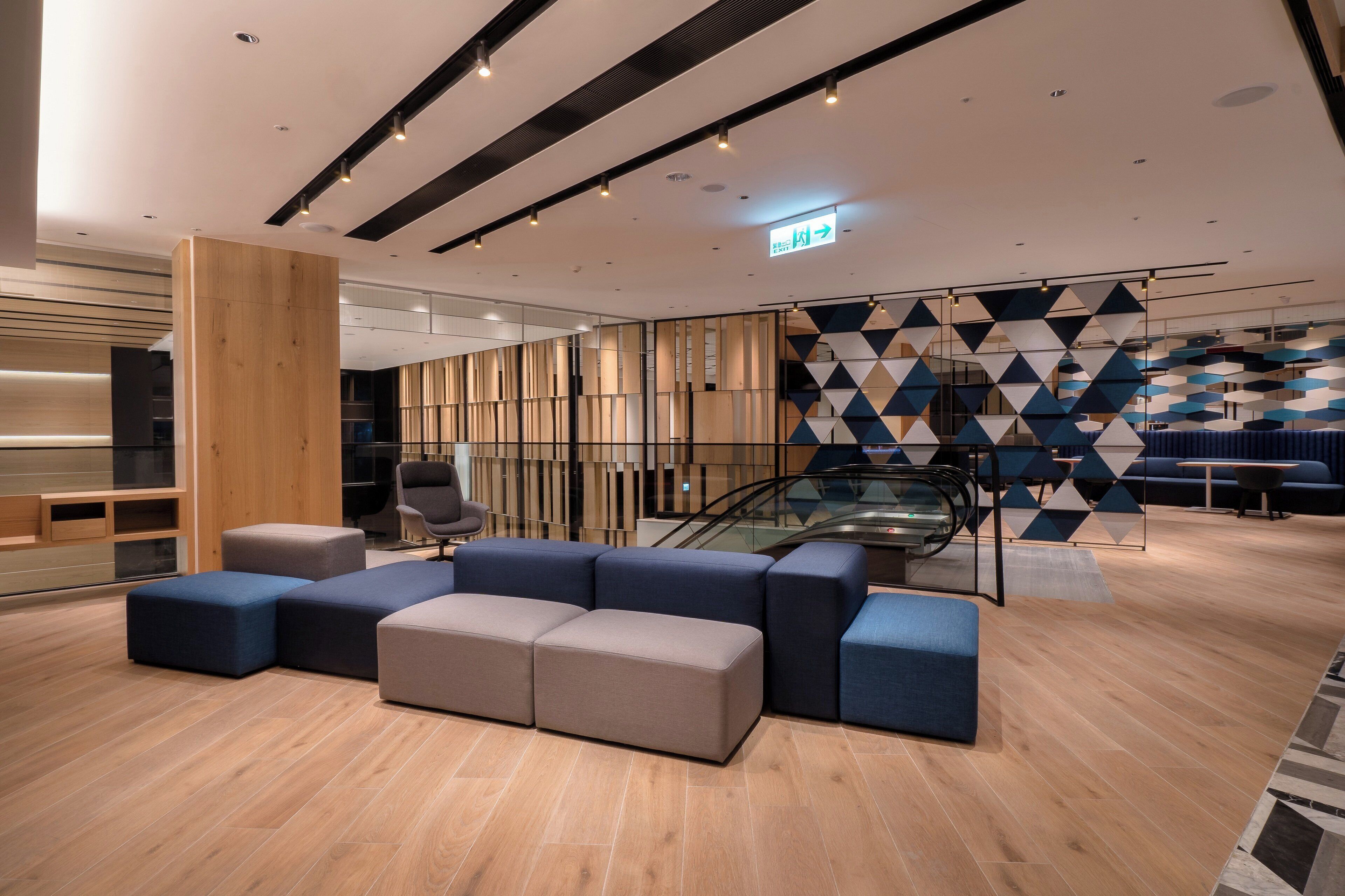 A modern lobby with a seating area, a staircase, and a geometric patterned wall.