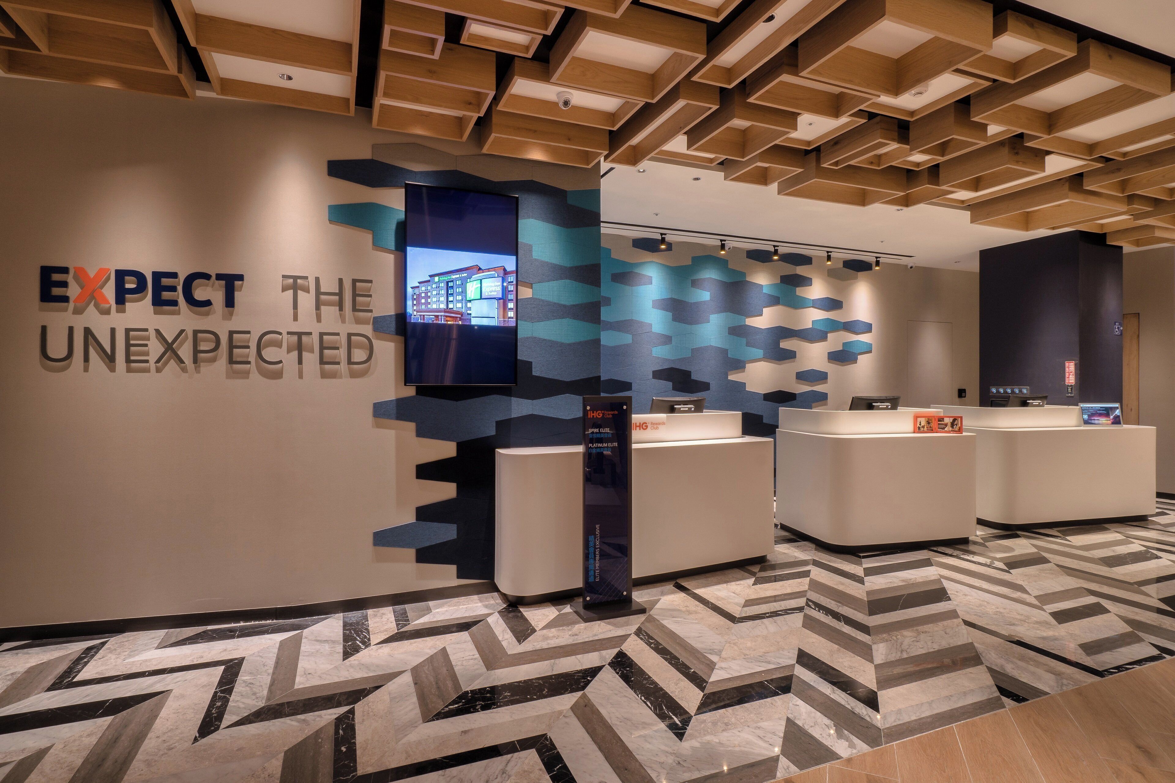 A reception area with a modern design, including a wall-mounted TV, a reception desk, and a patterned floor.