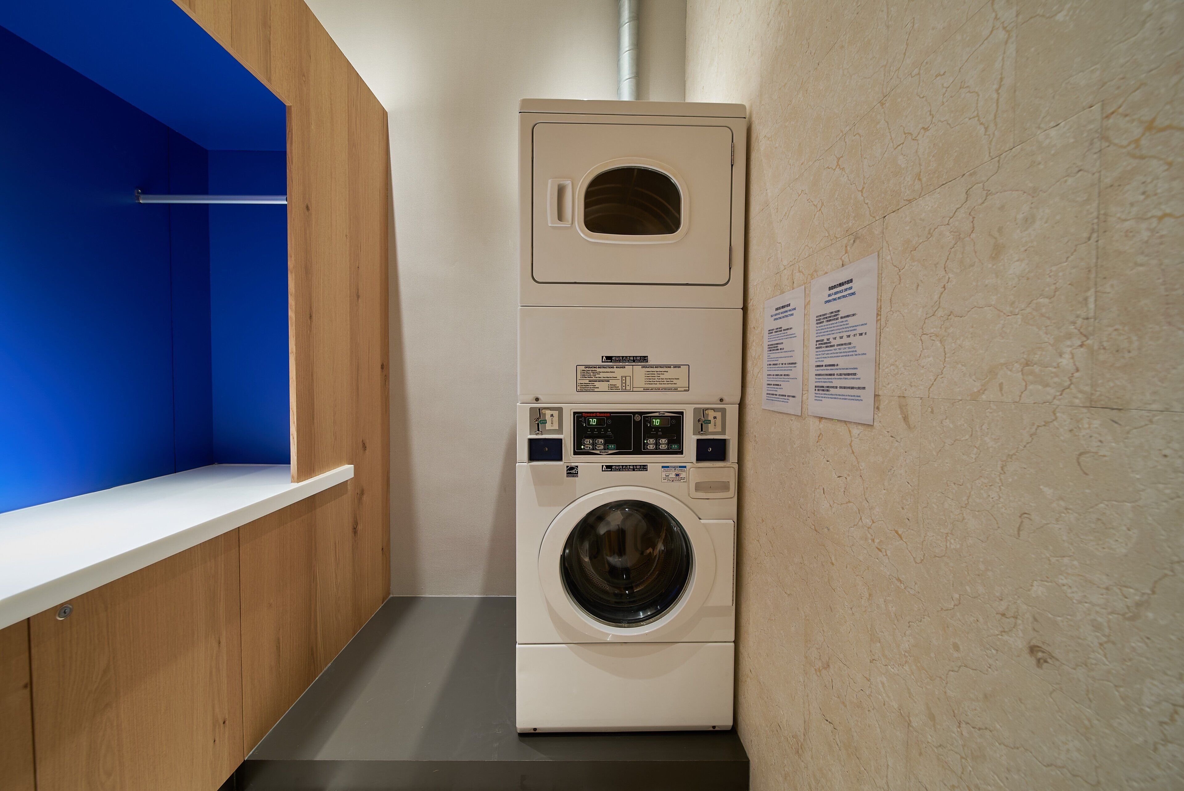 Un lavadero pequeño y moderno con lavadora y secadora integradas, un banco de madera y una pared azul.