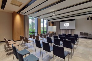 Une salle de conférence avec des rangées de chaises, un écran de projection et une grande fenêtre donnant sur un paysage verdoyant.
