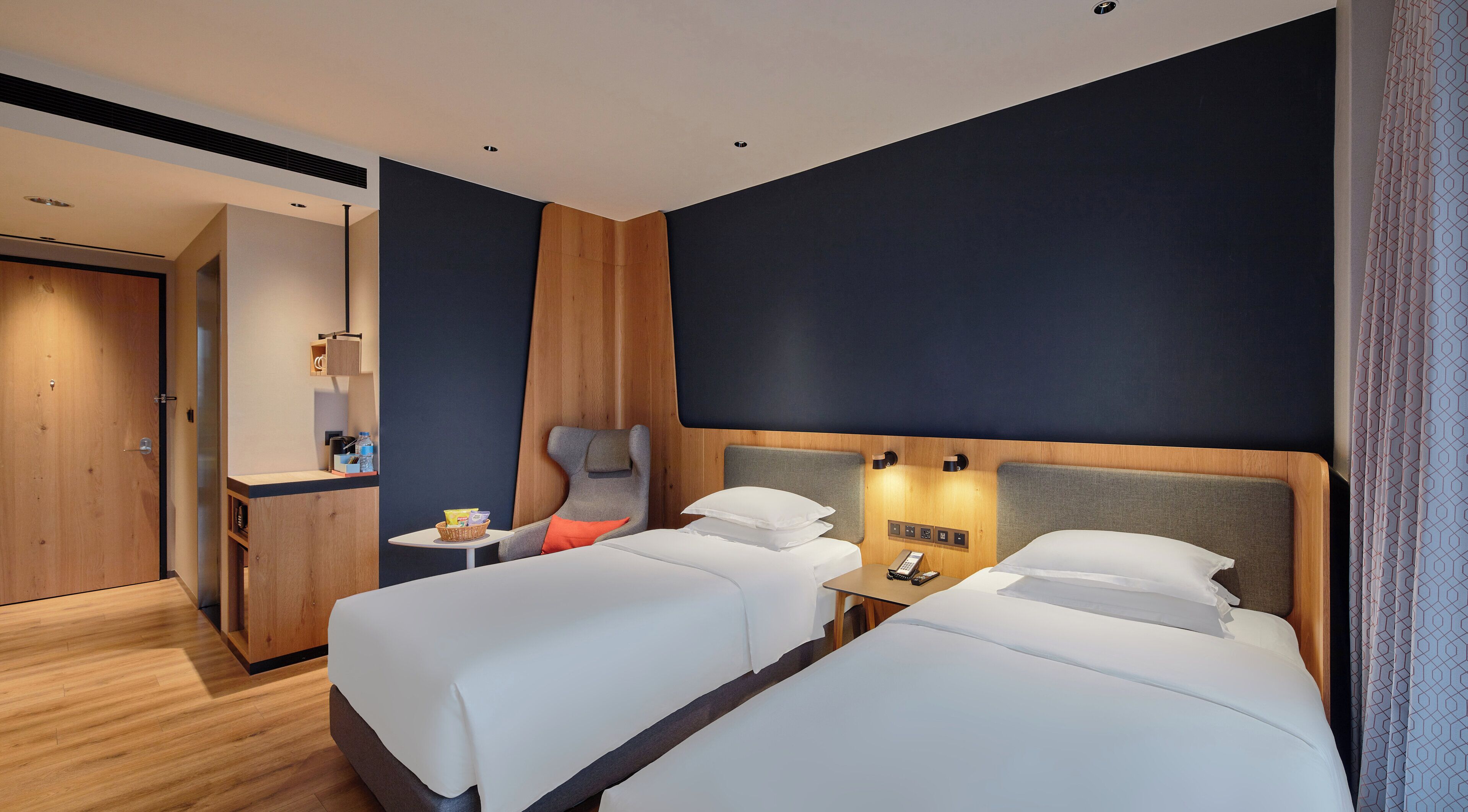 Habitación de hotel con dos camas, un escritorio, una silla y una mesita con una cesta.