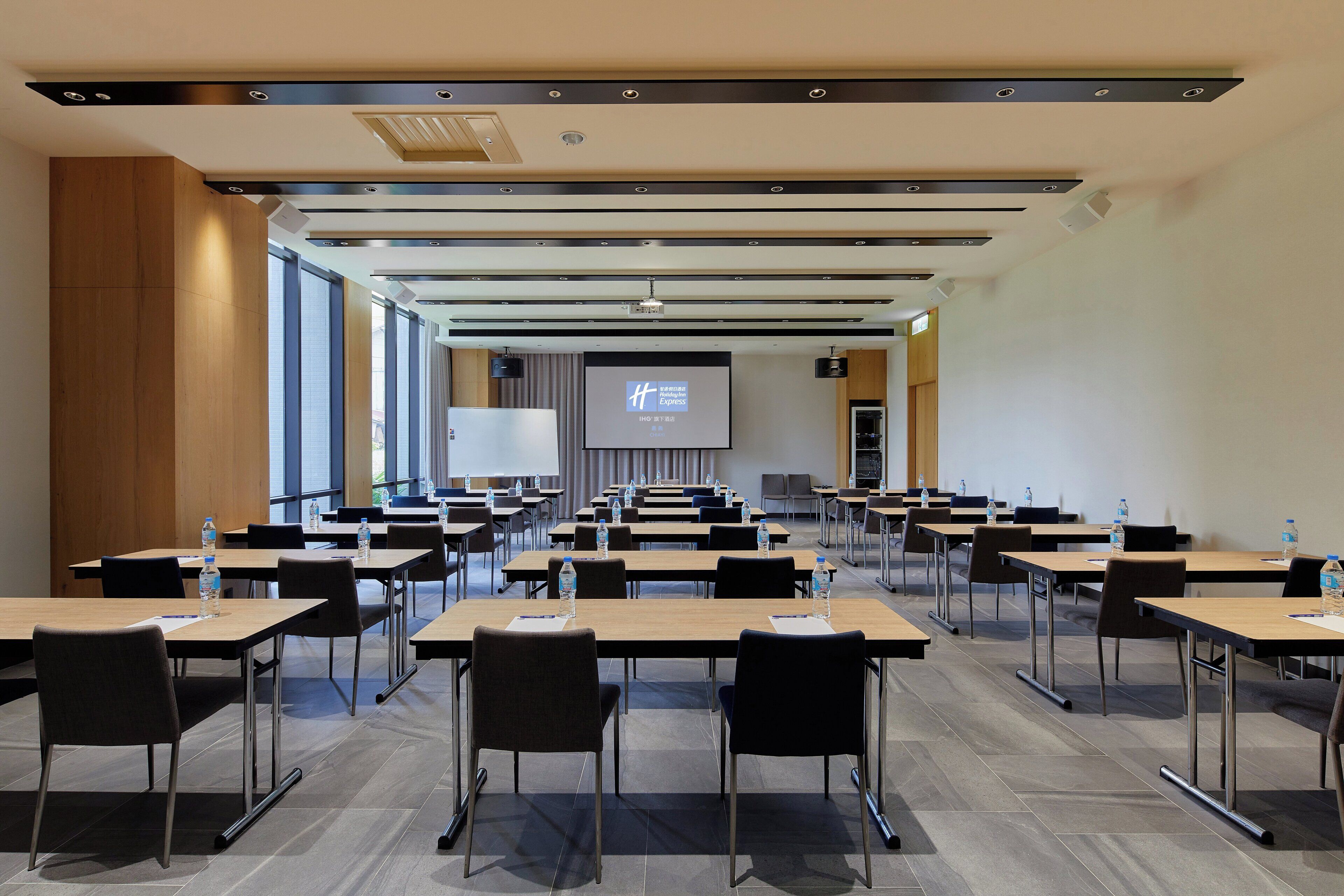 Uma sala de conferências com várias mesas e cadeiras, um ecrã grande e um projetor.