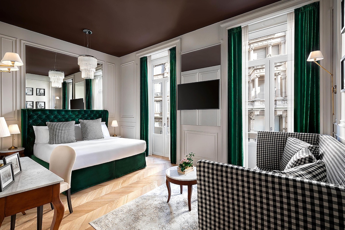 A hotel room with a large bed, a sofa, a small table, and a TV.