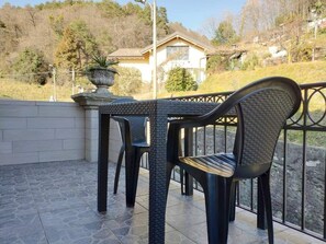 Eine Terrasse mit Tisch und Stühlen, ein Steinfußboden und Blick auf ein Haus im Hintergrund.