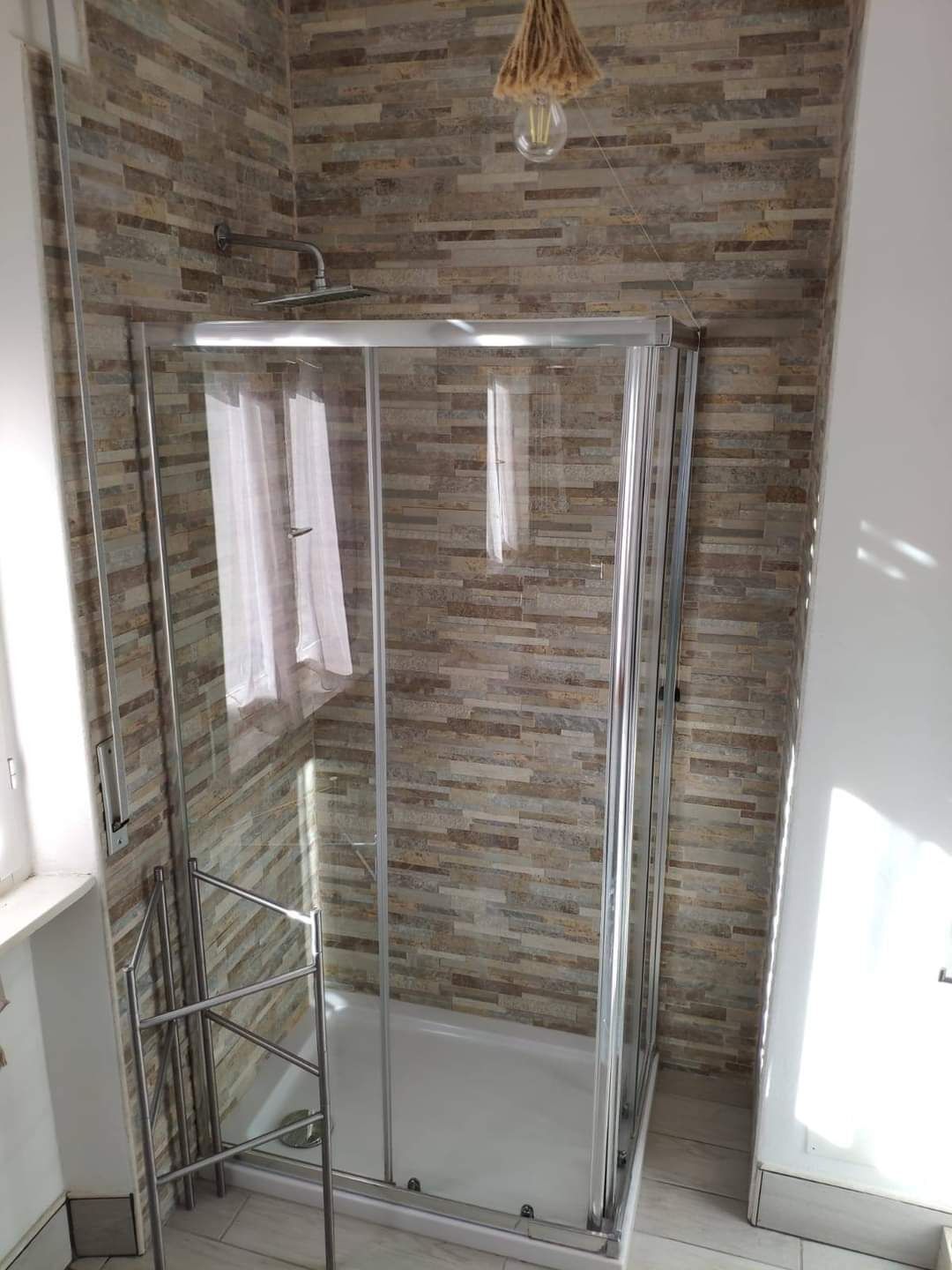 Eine gläserne Dusche mit Metallrahmen, einem Handtuchhalter und einer hängenden Leuchte.