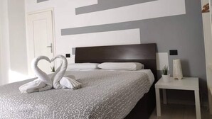 Una habitación de hotel con cama, mesita de noche, lámpara en la pared y un panel decorativo.