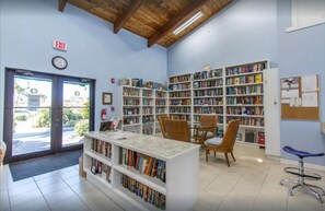Interior de biblioteca com estantes, um relógio e uma porta com sinalização de saída.
