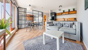 A modern living room with a grey sofa, a white coffee table, and a dining area with a wooden table and chairs. - Apartamenty Sun & Snow Waterlane Island (Gdansk)