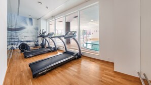 A gym with treadmills, a rowing machine, and a glass wall with a pool view. - Apartamenty Sun & Snow Waterlane Island (Gdansk)