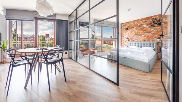 A modern bedroom with a large bed, a glass wall, and a view of the city. - Apartamenty Sun & Snow Waterlane Island (Gdansk)