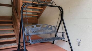 Een metalen bank met metalen frame, geplaatst nabij een trap met houten treden en een metalen leuning.