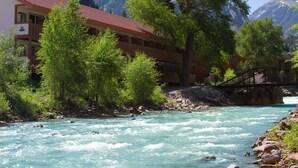 A hotel with a red roof, surrounded by lush greenery and a river. - Hot Springs Inn (Ouray)
