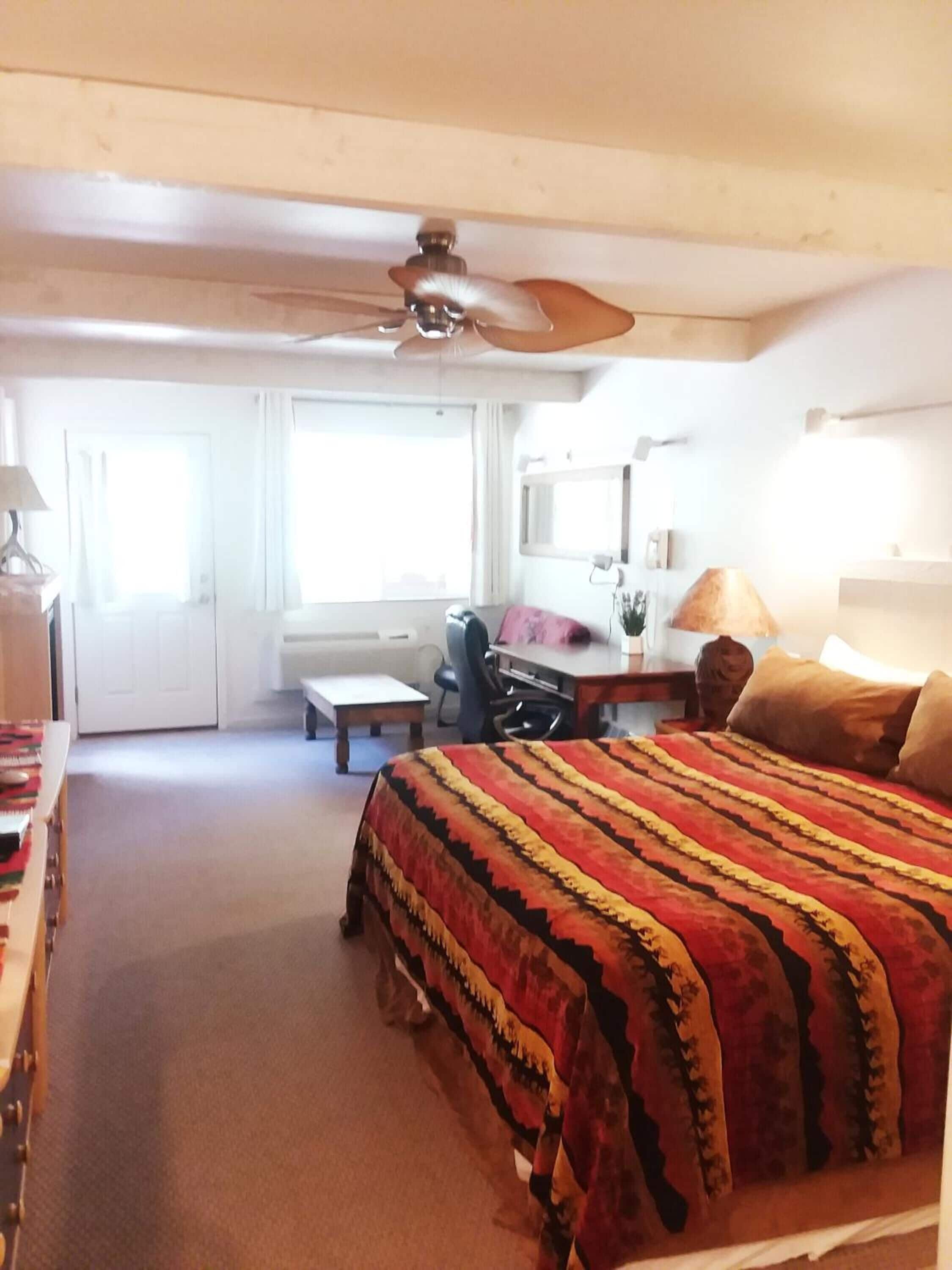 A hotel room with a bed, desk, chair, and a ceiling fan.