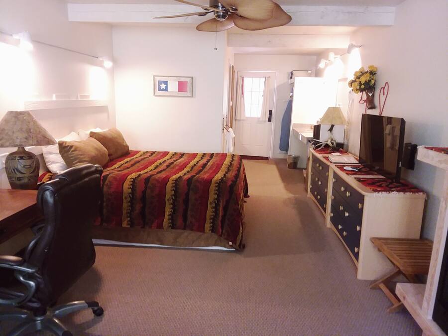 Ein Schlafzimmer mit Bett, Schreibtisch, Stuhl, Kommode, Deckenventilator und einer Wand mit Flagge und Blumenvasen.