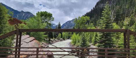 A wooden bridge over a river with a mountainous backdrop.