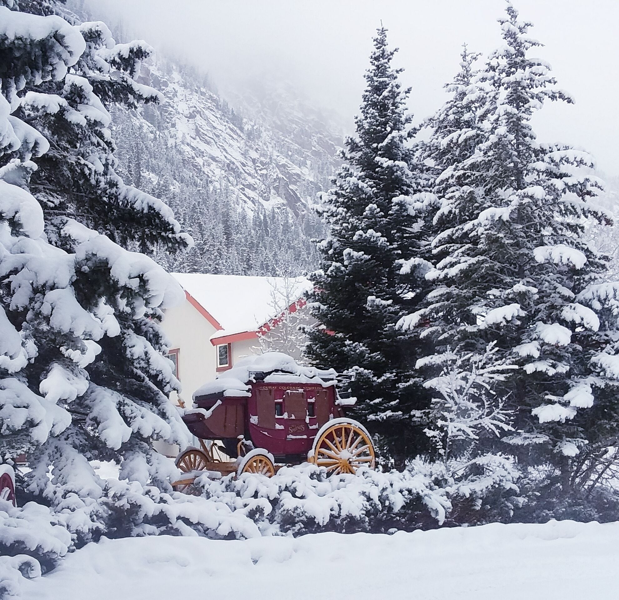 A snow-covered landscape with a building and a horse-drawn carriage.
