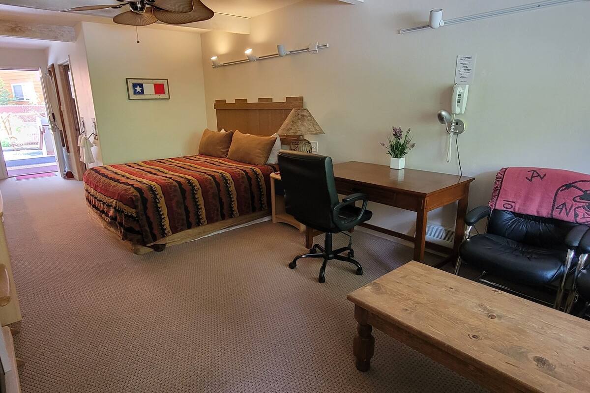 A room with a bed, desk, chair, and sofa. There is a flag on the wall and a telephone on the desk.