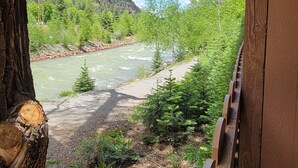 A wooden deck overlooking a river with a forested hillside in the background. - Hot Springs Inn (Ouray)