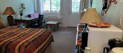 A hotel room with a bed, a desk, a chair, a coffee maker, and a window.