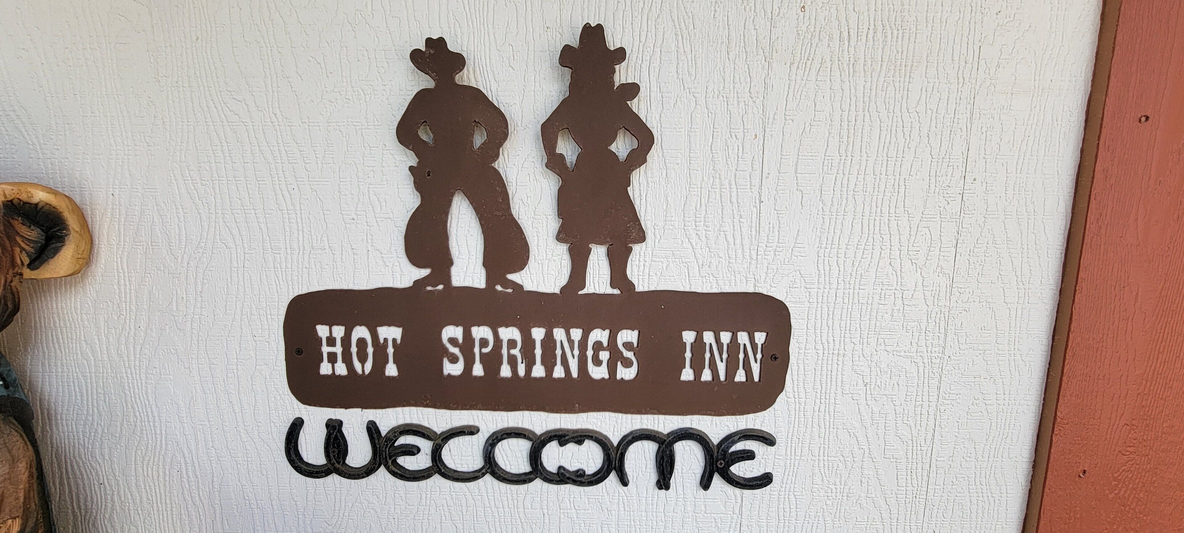 Sinal com silhuetas de duas pessoas e os dizeres 'HOT SPRINGS INN' e 'BEM-VINDO'.