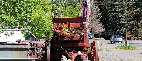 Ein alter Traktor mit amerikanischer Flagge, geparkt auf einem Kiesgrund mit Bäumen und einem Berg im Hintergrund.
