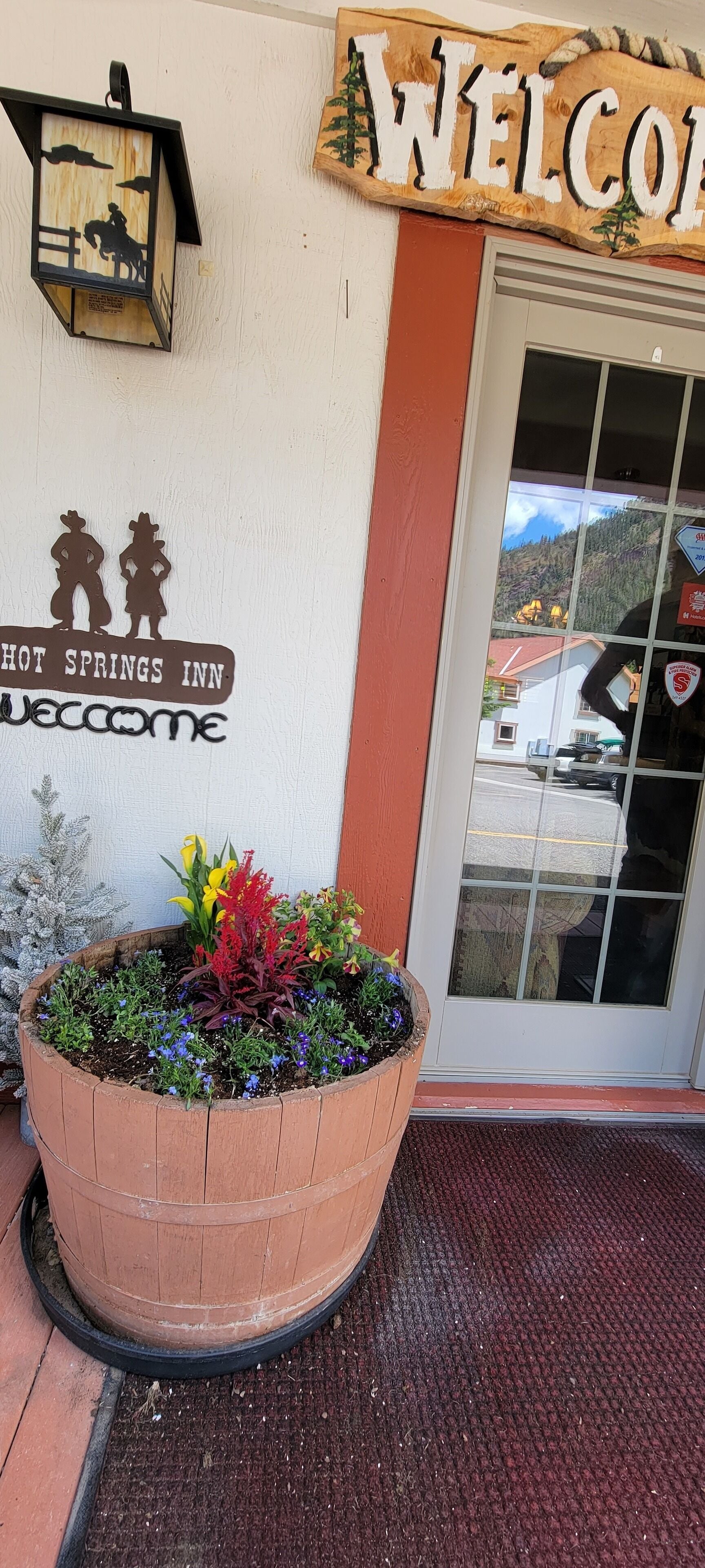 Un letrero de madera con la inscripción "HOT SPRINGS INN" y "BIENVENIDOS" sobre una puerta.