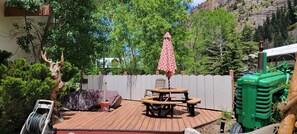 A wooden deck with picnic tables and an umbrella, surrounded by lush greenery and a white fence. - Hot Springs Inn (Ouray)