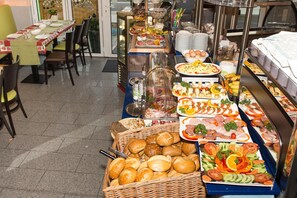 Ein reichhaltiges Buffet mit verschiedenen Speisen und eine Sitzgelegenheit mit Tischen und Stühlen.