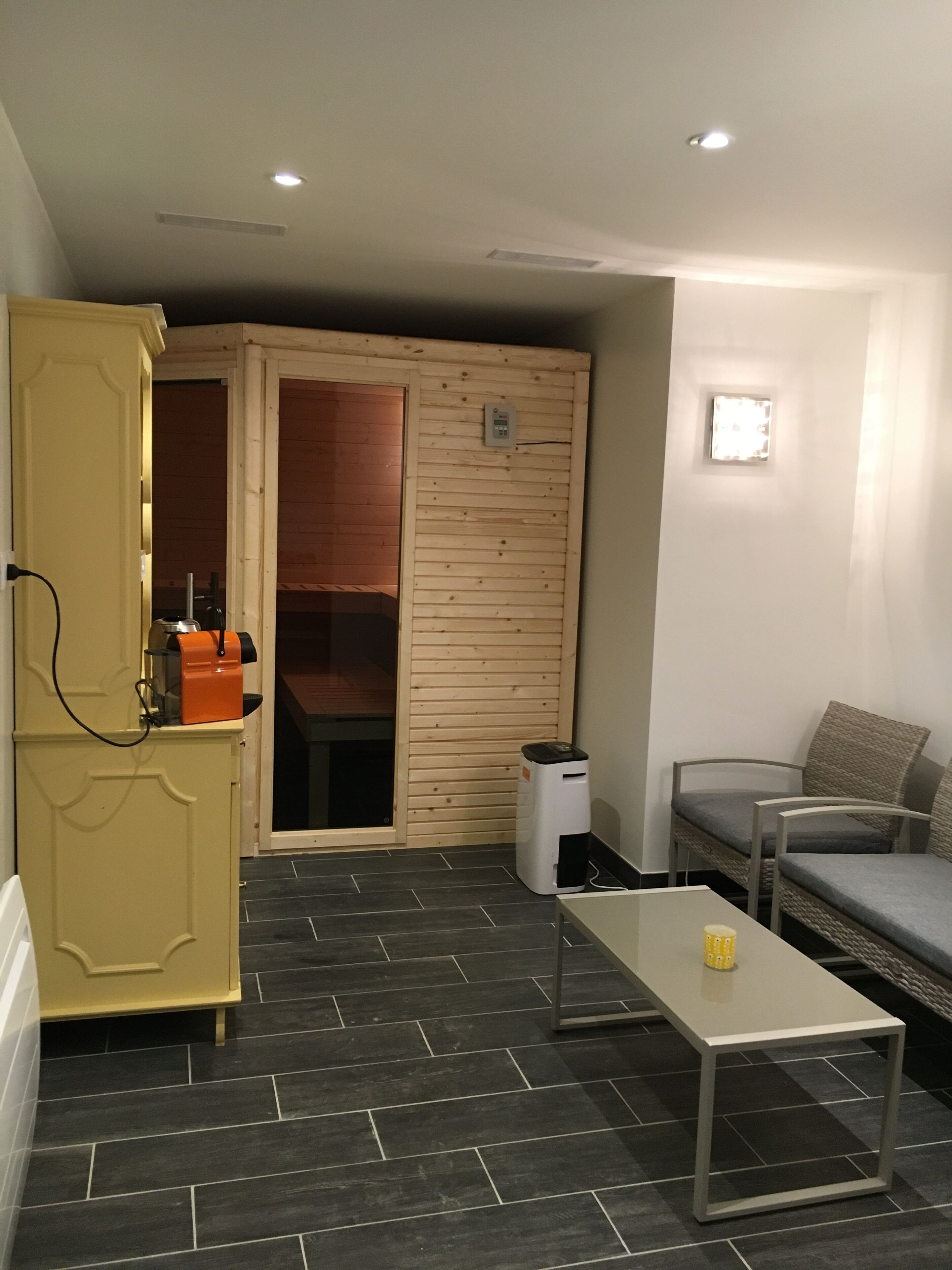 A compact living space with a kitchenette, a seating area with a sofa and armchairs, a small table, and a sliding door leading to a bathroom.