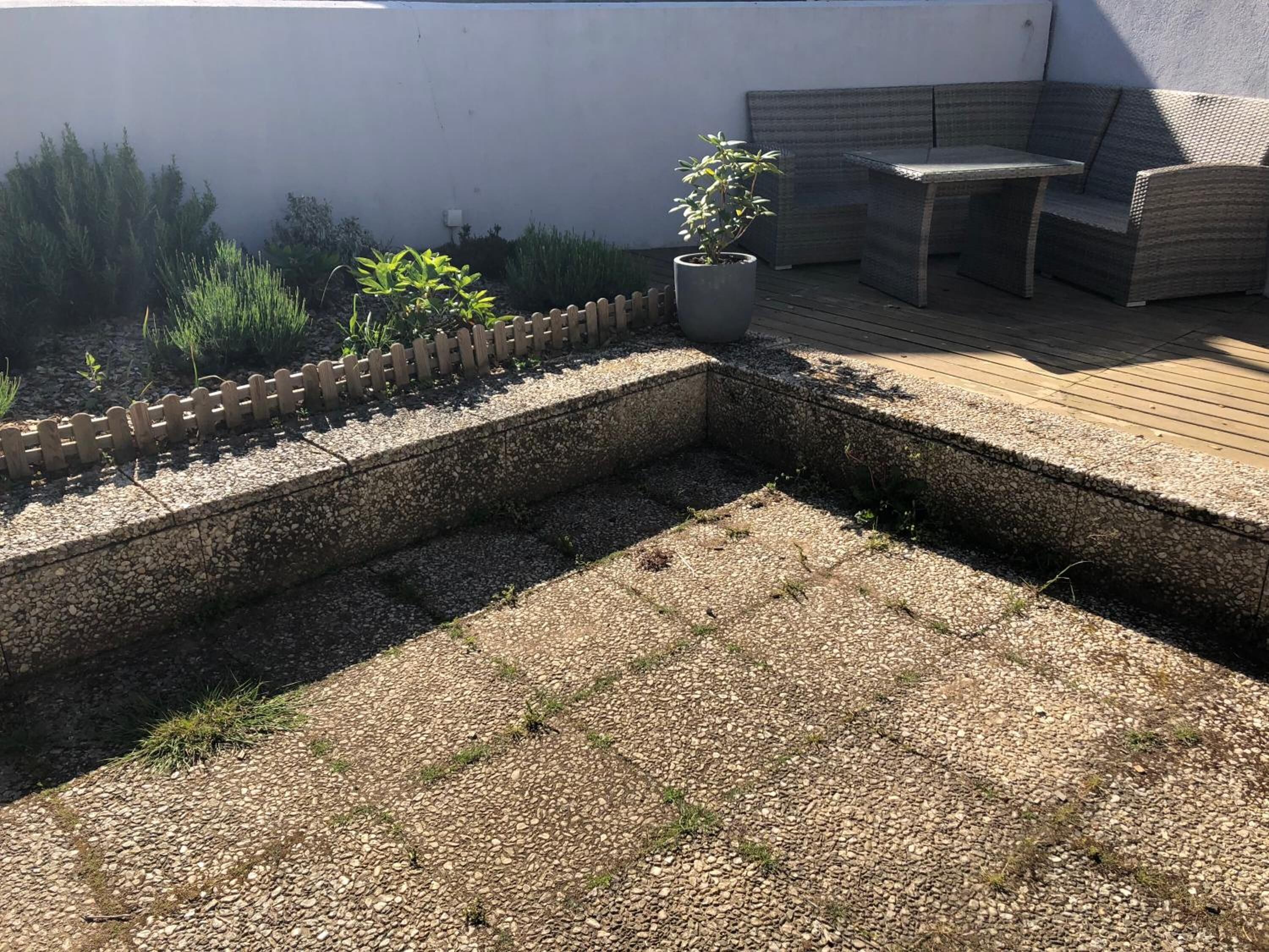 A patio area with a wooden deck, a seating area with a table and chairs, and a small garden with a potted plant.