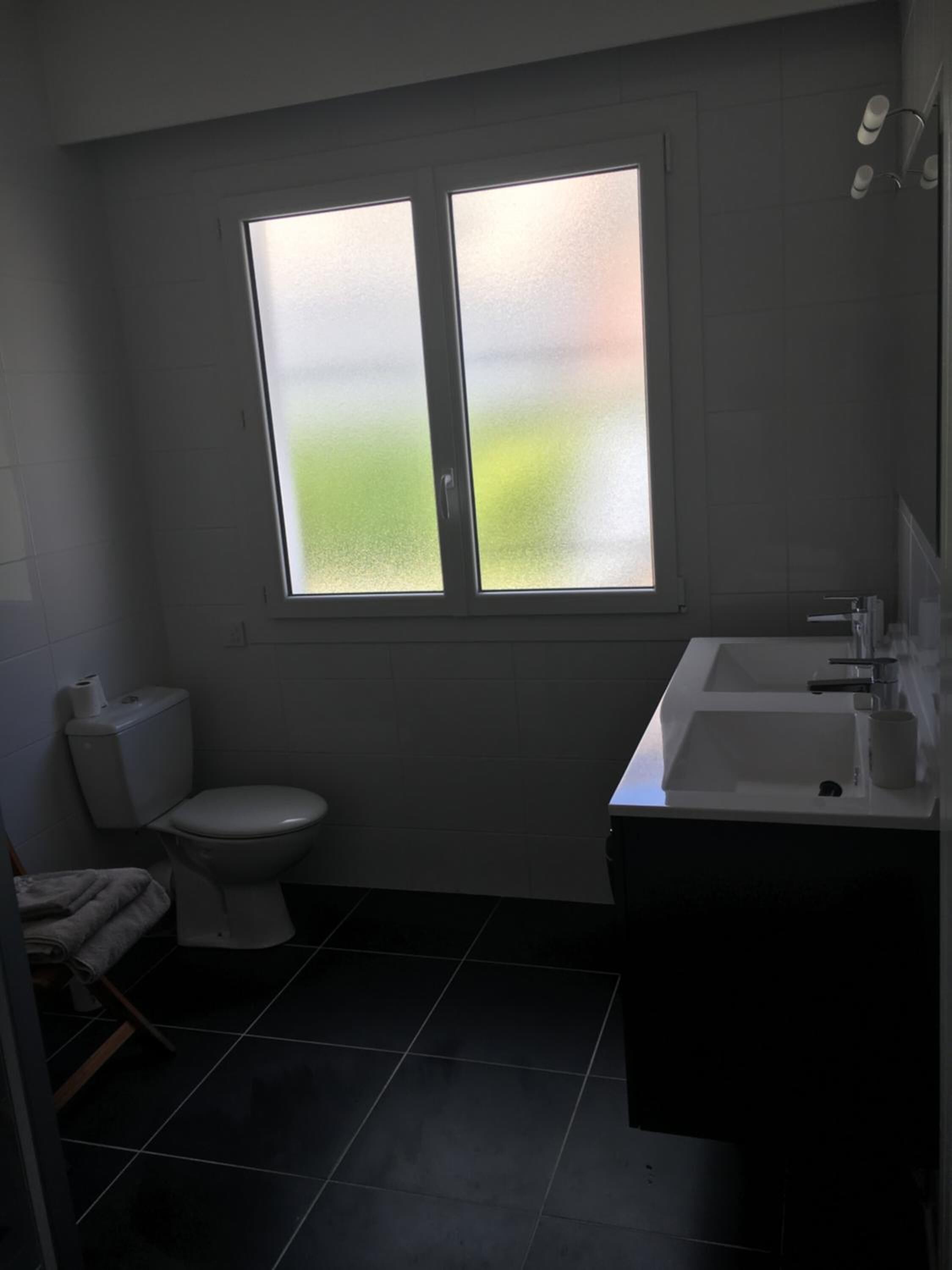 A small, modern bathroom with a toilet, sink, and window.