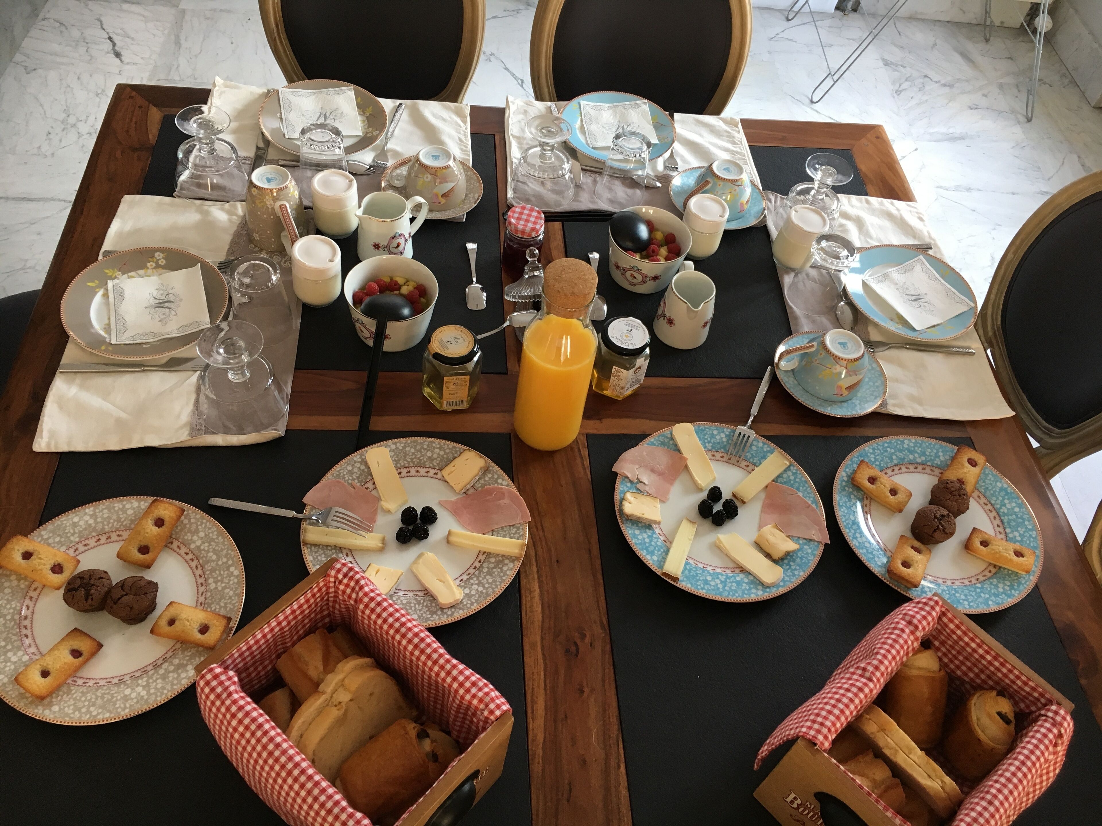 Une table en marbre dressée pour le petit-déjeuner, avec des assiettes remplies de nourriture, un pichet de jus d’orange et divers autres aliments typiques du petit-déjeuner.