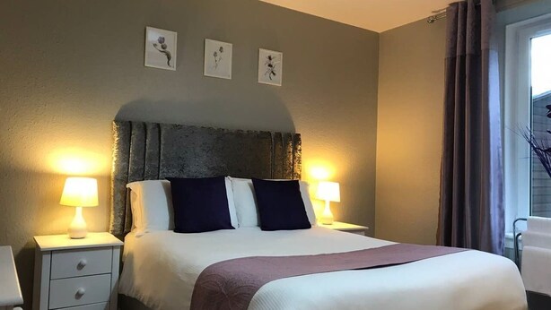 Ein ordentlich gemachtes Bett mit Kopfteil, zwei Nachttische mit Lampen und drei gerahmte Bilder an der Wand.