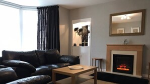 Ein Wohnzimmer mit einem schwarzen Ledersofa, einem Holztisch, einem Kamin und einem Spiegel an der Wand.