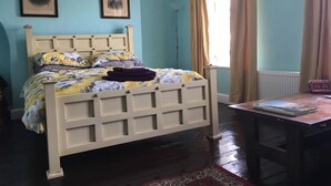 A bedroom with a bed, two framed pictures on the wall, a window with curtains, and a table with a book. - St Nicholas Street Apartment (Bristol)