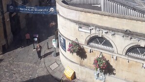 A historic building with a curved facade, a sign for St. Nicholas Markets, and hanging flower baskets. - St Nicholas Street Apartment (Bristol)