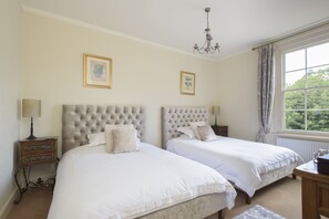 A bedroom with two beds, a chandelier, framed artwork, and a window with curtains. - Sissinghurst Castle Farmhouse (Cranbrook)