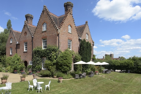 A large brick building with a garden patio featuring outdoor furniture and umbrellas.