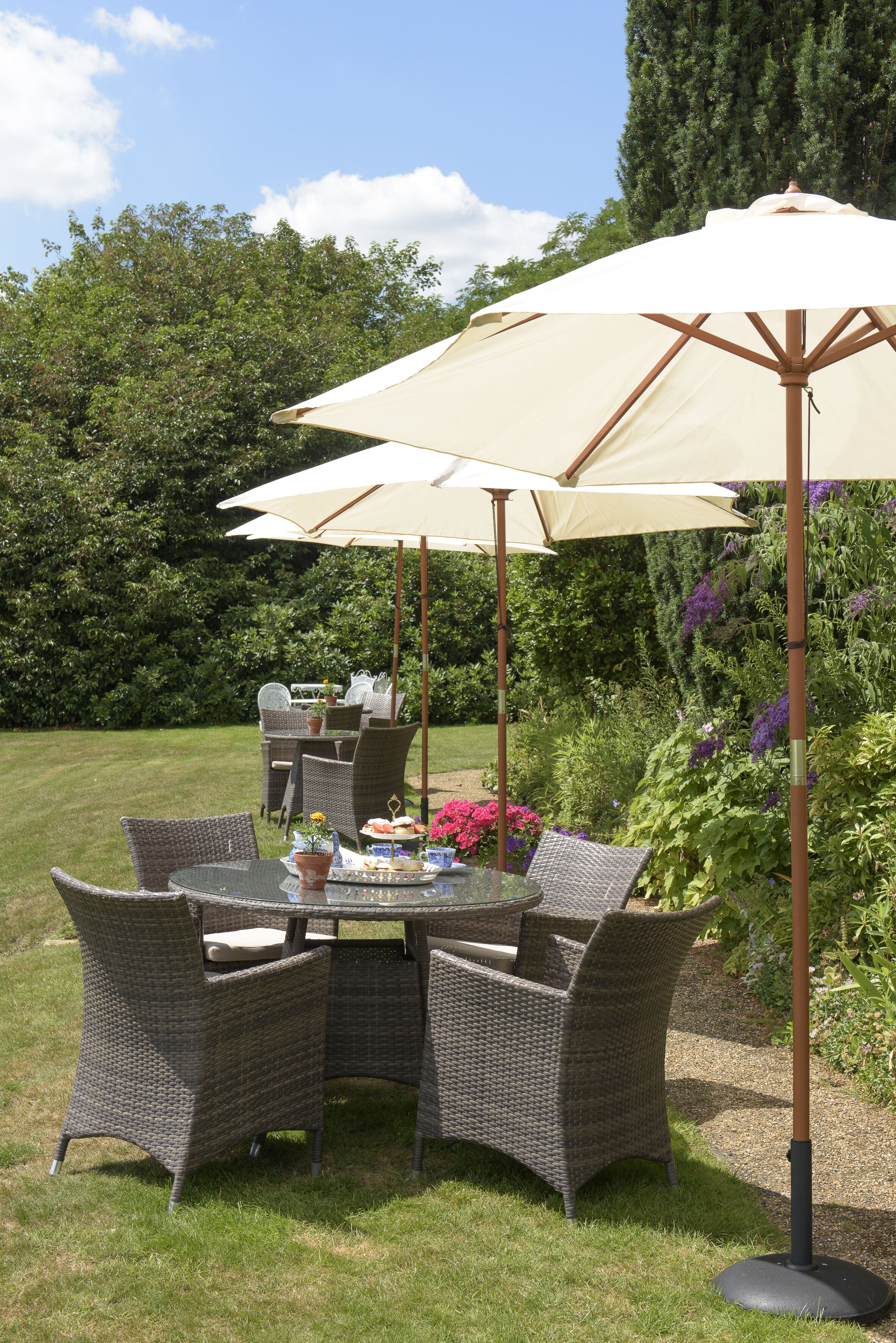 Et rundt bord med fletstole og en stor parasol i en have.