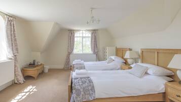 A bedroom with two single beds, a wooden headboard, bedside tables with lamps, a window with curtains, and a radiator.
