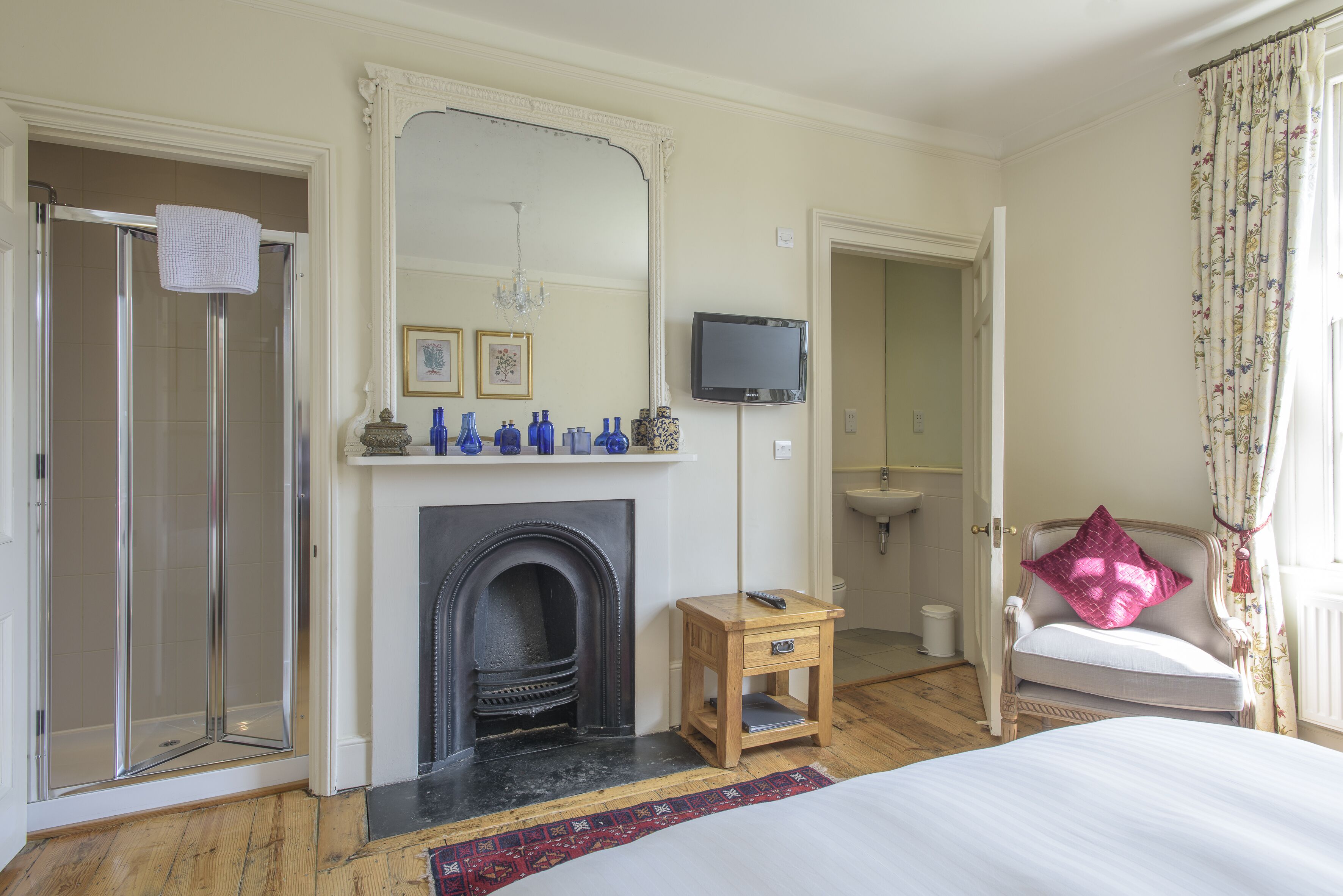 A bedroom with a glass shower, a fireplace, a television, and a bed.