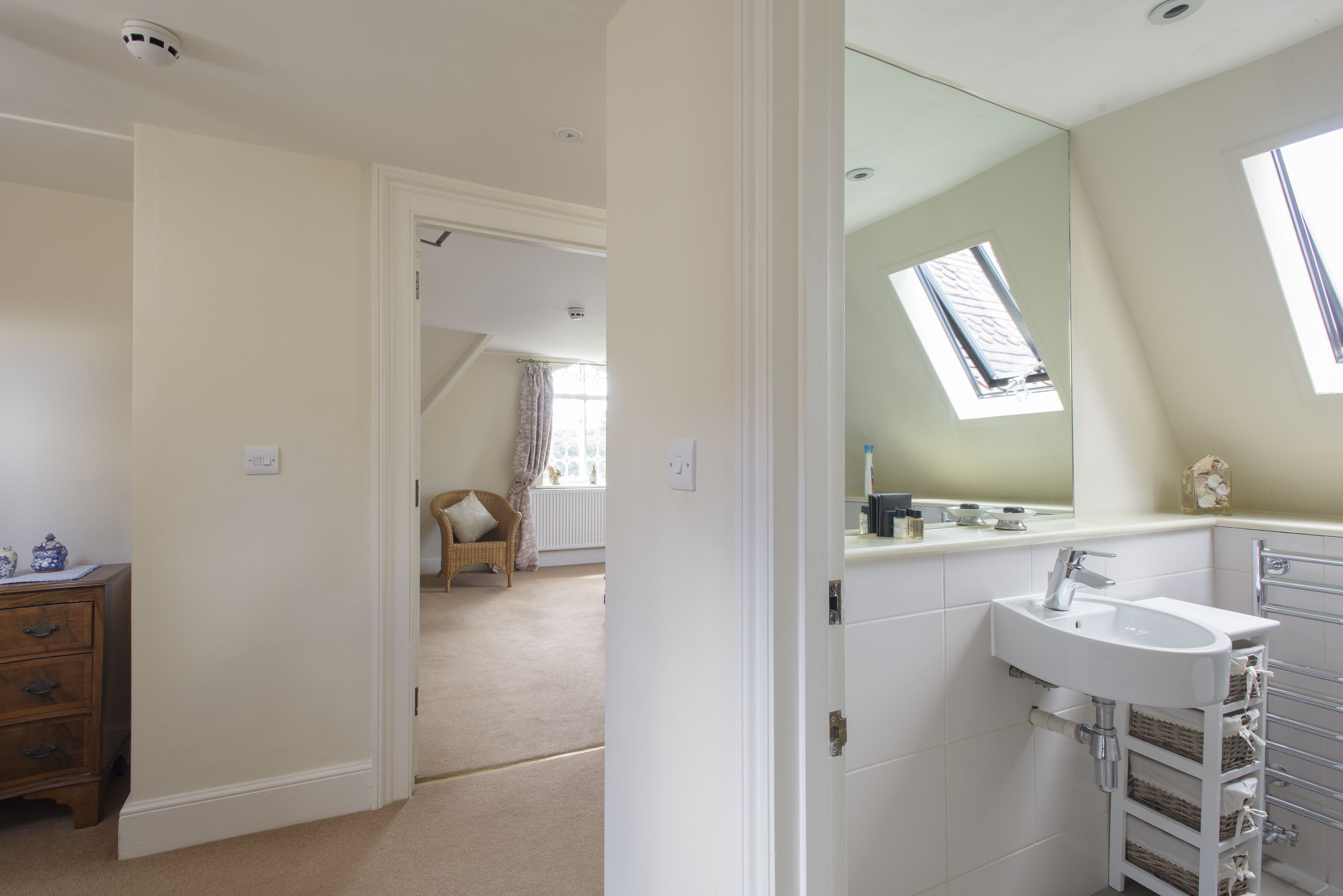 A bedroom with a large window, a white dresser, and a bathroom with a sink and mirror.