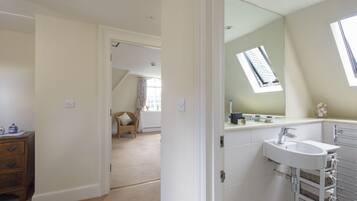 A bedroom with a large window, a white dresser, and a bathroom with a sink and mirror.