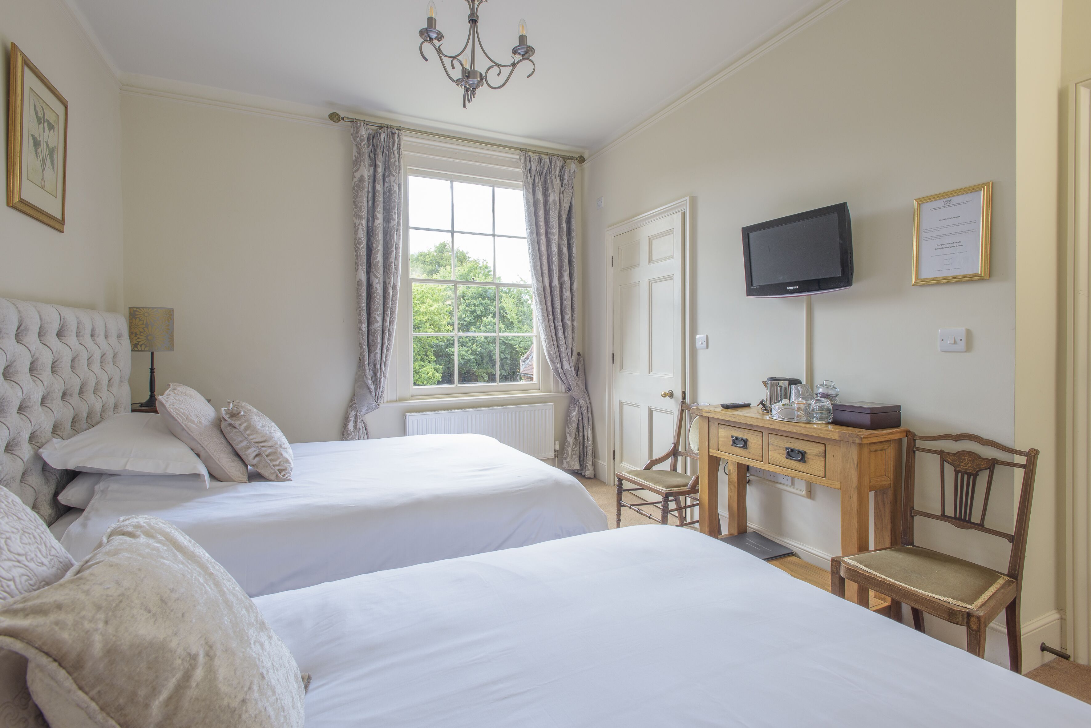 A hotel room with two beds, a desk with a chair, a television, and a window with curtains.