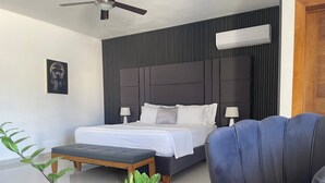 Un dormitorio moderno con una cama grande, una mesita de noche, una silla, un ventilador de techo y un aire acondicionado.