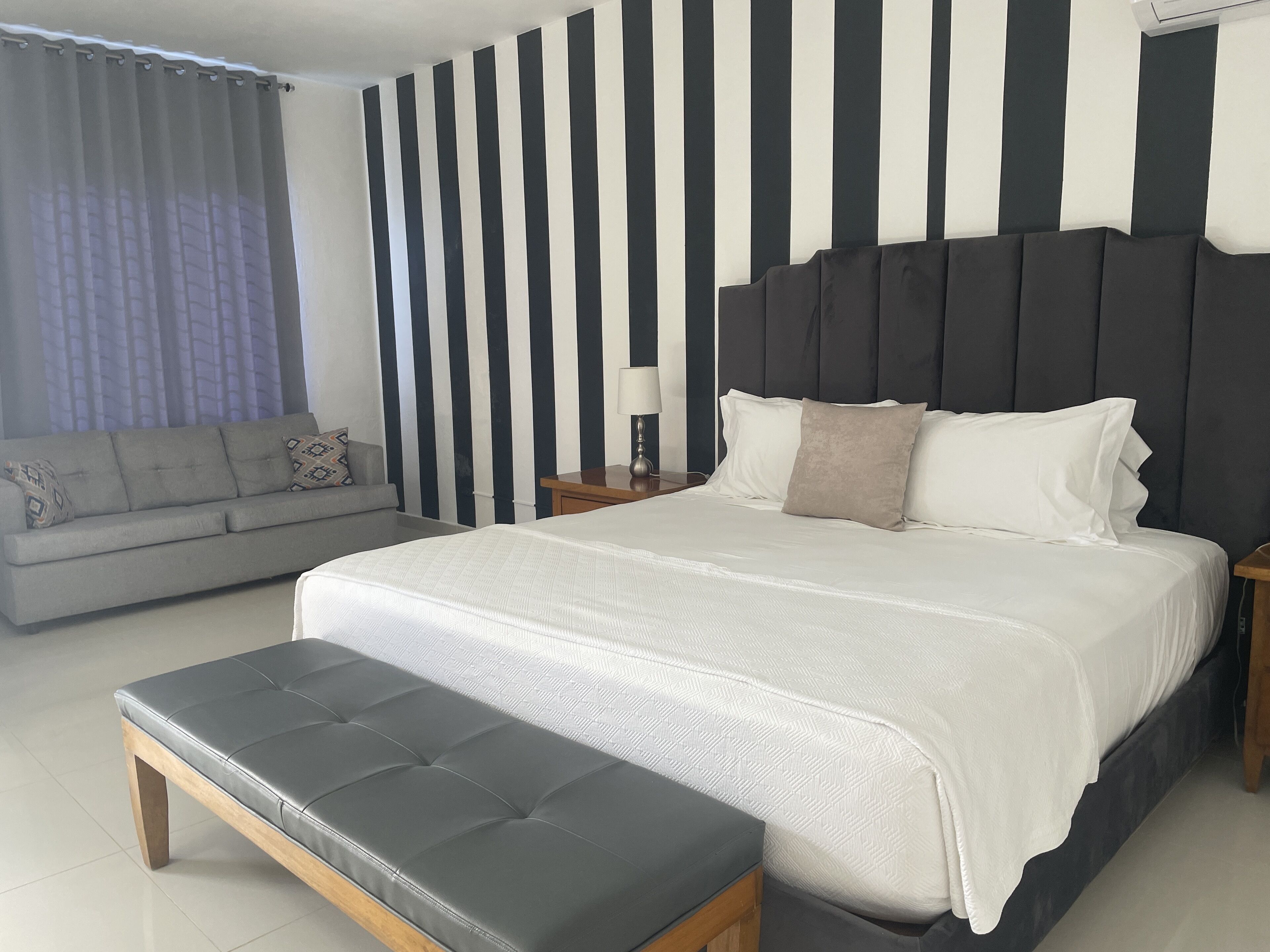 A modern bedroom with a large bed, a grey sofa, and a striped wall.