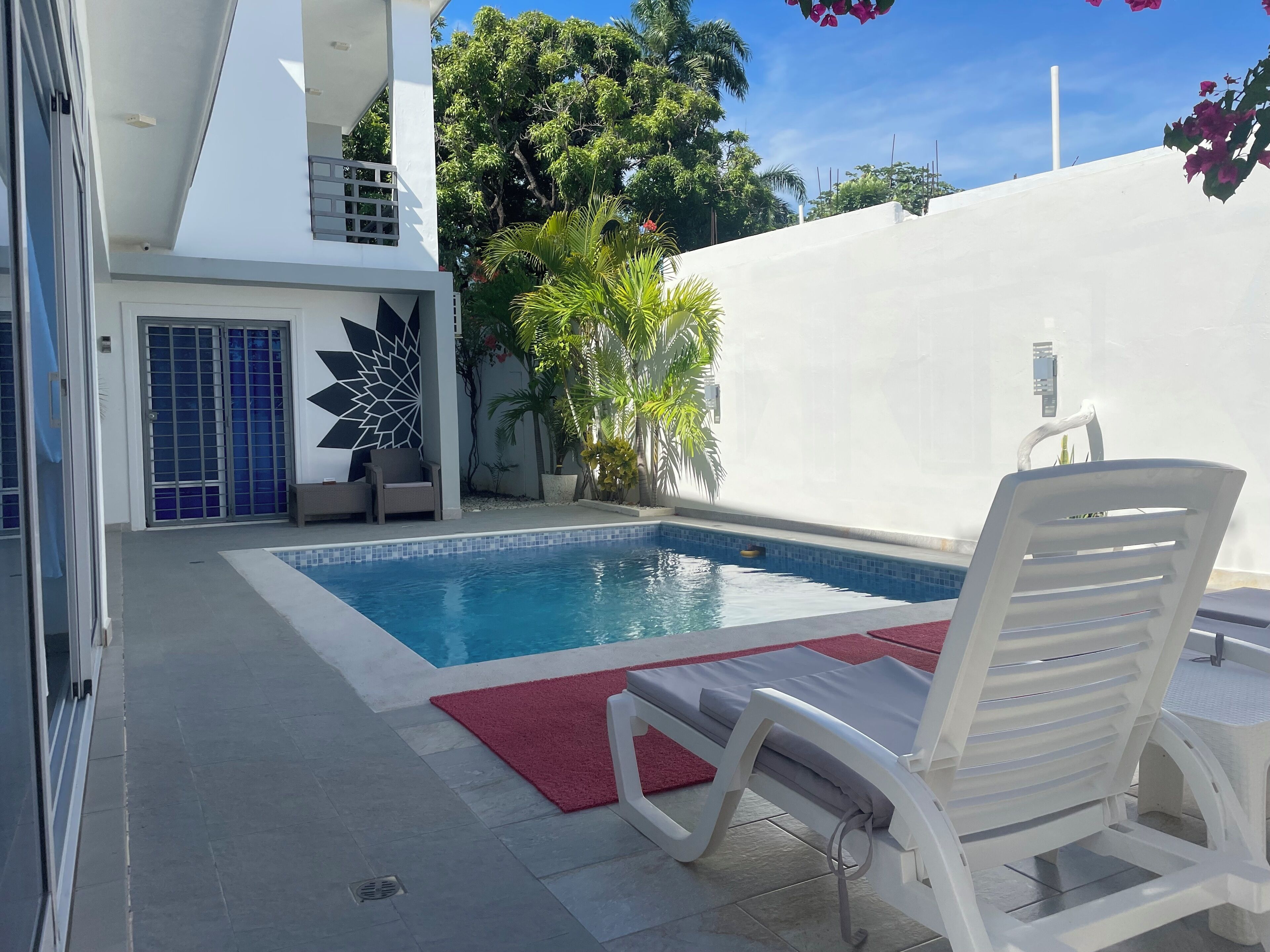 A swimming pool with a red mat, a white lounge chair, and a geometric wall design.