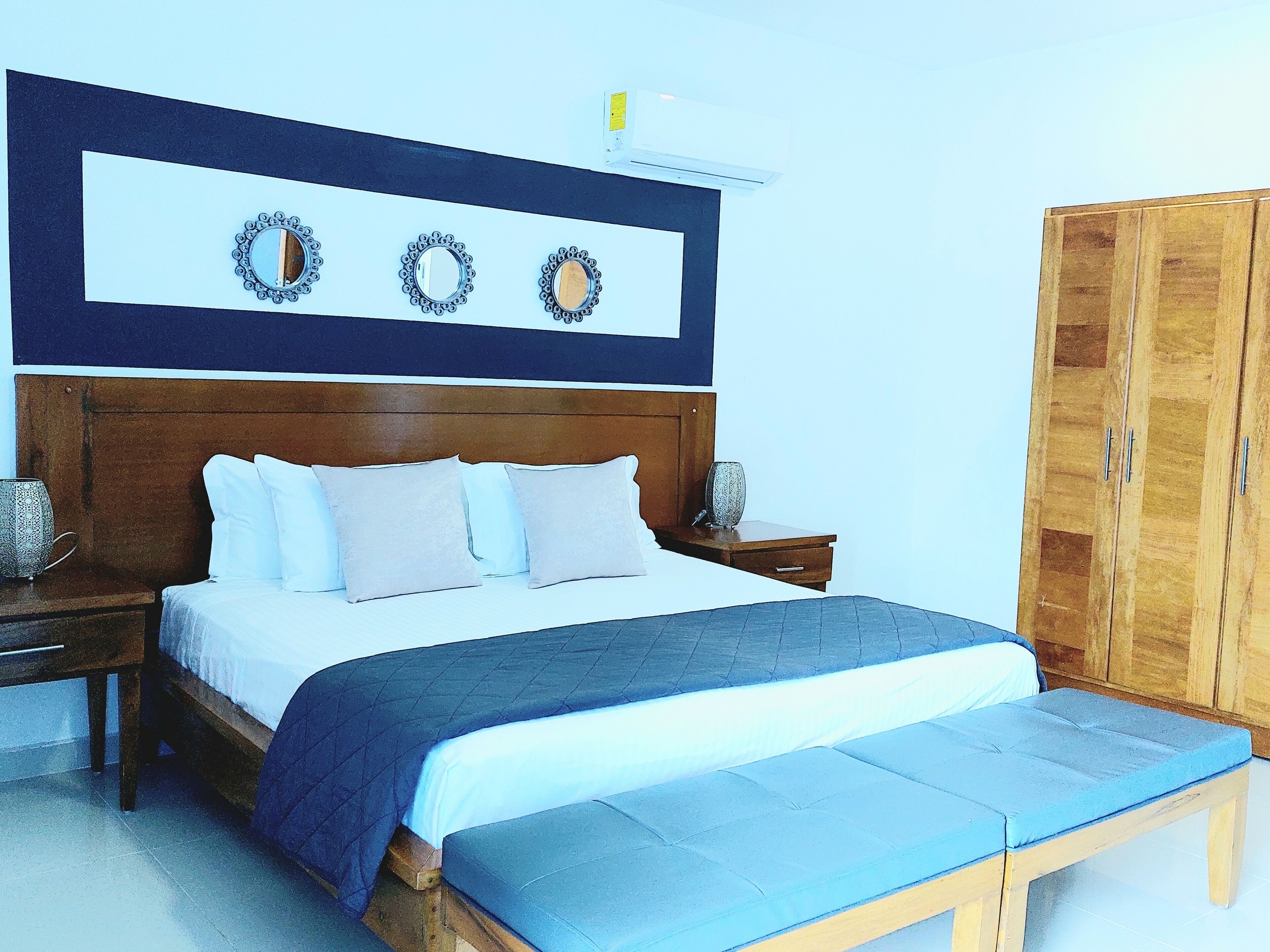 A bedroom with a wooden headboard, a bed with white bedding, a blue bench, and a wardrobe.