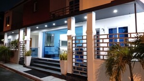 Un edificio de dos pisos con una entrada bien iluminada, una escalera que conduce a la puerta principal y un balcón en el nivel superior.